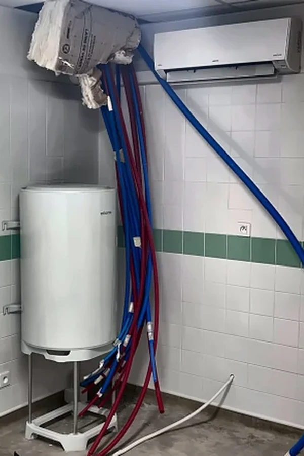 Ballon d'eau chaude sanitaire sur trépied avec raccordements de plomberie en cours d'installation dans une école maternelle à Saint-Laurent-Nouan (41).