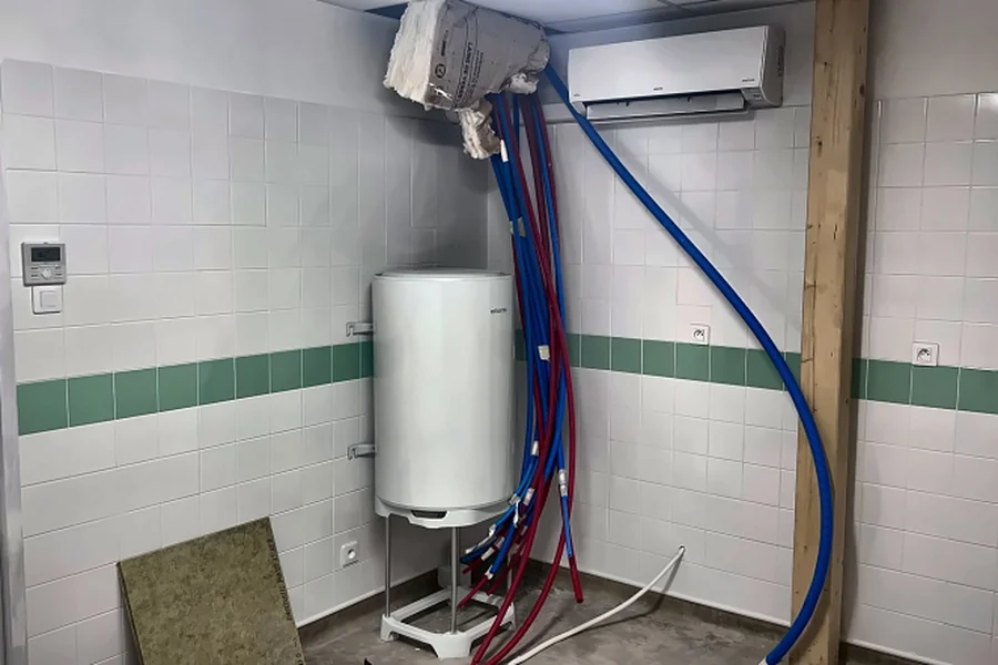Ballon d'eau chaude sanitaire sur trépied avec raccordements de plomberie en cours d'installation dans une école maternelle à Saint-Laurent-Nouan (41).