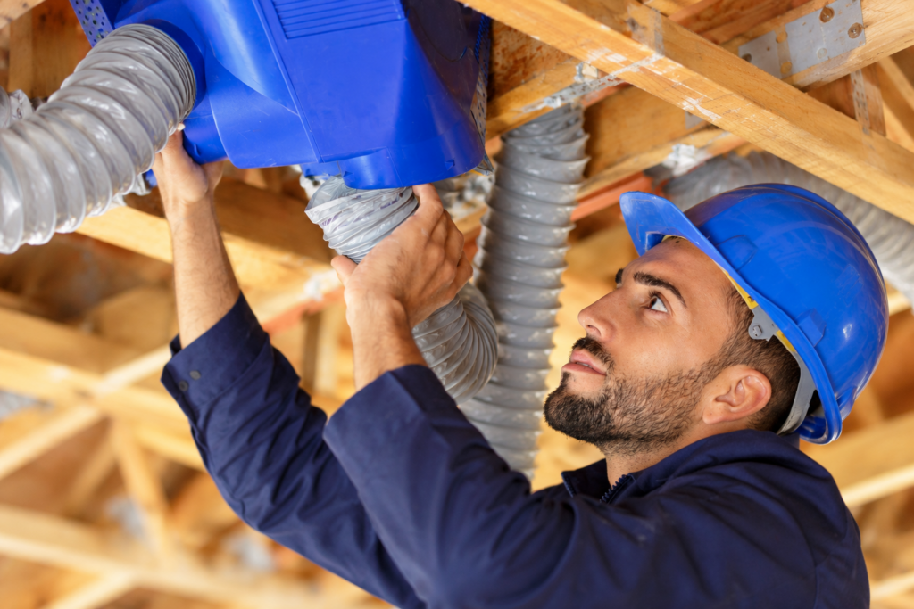 Artisan installant une VMC et raccordant les gaines de ventilation dans les combles d’une maison.